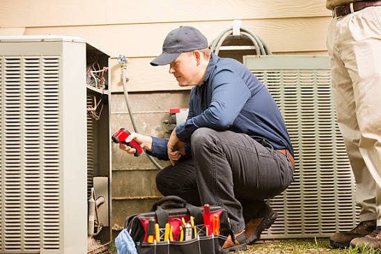 Technician inspecting an outdoor HVAC condenser beside a house
